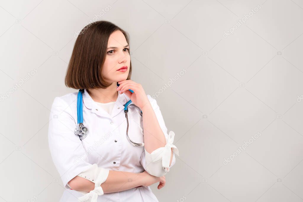 Portrait of beautiful young doctor with pensive face on light background