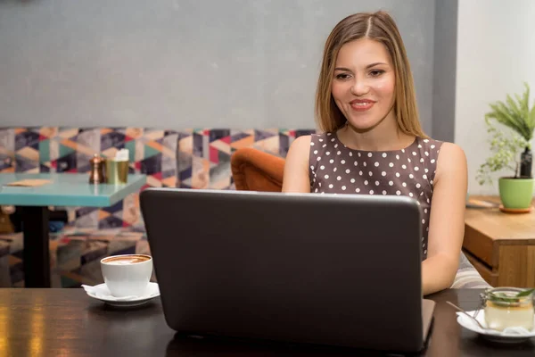 Joven hermosa mujer rubia sonriente trabaja en el ordenador portátil en la cafetería — Foto de Stock