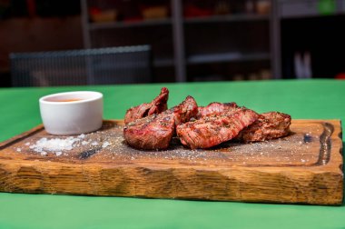 Ahşap bir mutfak tahtasına sosla süslenmiş ızgara sığır eti madalyonu.