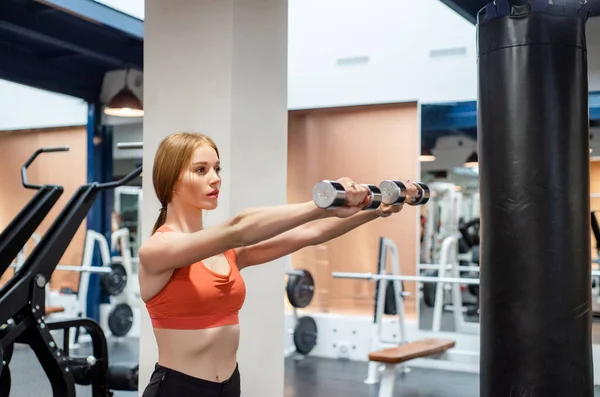 Beautiful young woman trains deltoid in gym with dumb-bell — ストック写真