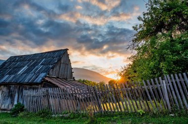 Evin üzerinde gün batımı ve kırsalda yeşil ağaçlar.