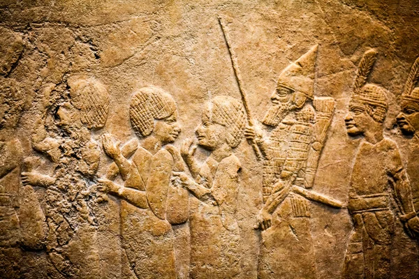 29. 07. 2015, Londra, İngiltere, British Museum - Asur duvarından arka planda Mısır binaları gösteren ayrıntılar. Ön planda, Nubia'lı mahkum tüy şapka giymek. — Stok fotoğraf