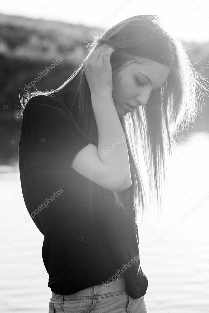 Black and white photo of beautiful girl with long, straight hair posing in the field with sunset light, against the light