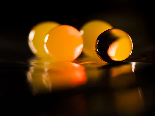 Abstract composition with beautiful, orange, round jelly balls on an aluminium foil with reflexions and dark background — Stock Photo, Image