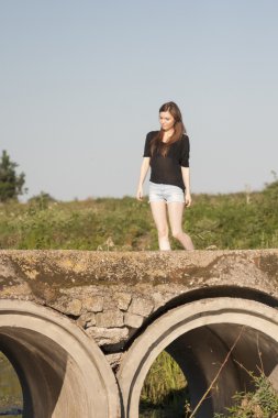 poz ve beton köprü üzerinde küçük bir nehir üzerinde oynama düz saçlı güzel kız