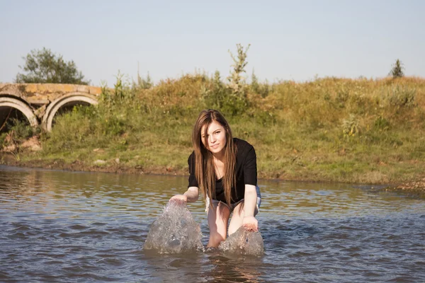 Beautiful girl with long, straight hair posing and playing with water in a small river — Stock Photo, Image