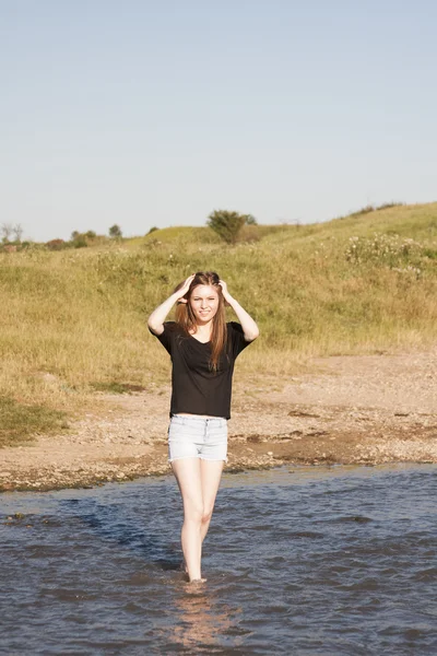 Hermosa chica con el pelo largo y liso posando y jugando con agua en un pequeño río — Foto de Stock