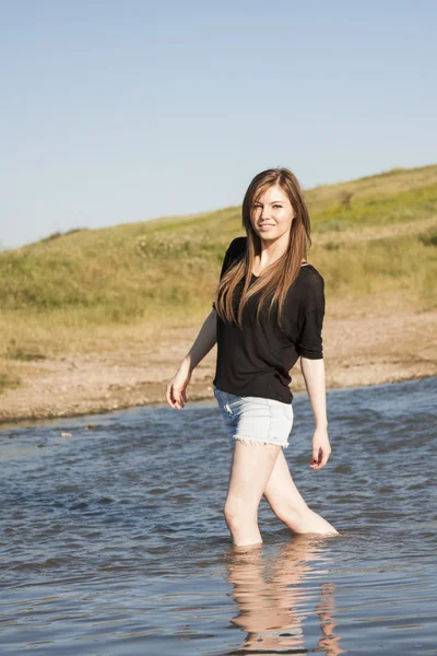 Beautiful girl with long, straight hair posing and playing with water in a small river — Stock Photo, Image