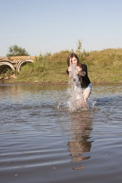 Beautiful girl with long, straight hair posing and playing with water in a small river — Stock Photo, Image