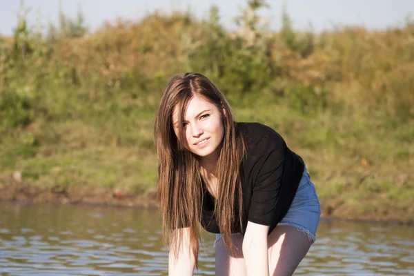 Hermosa chica con el pelo largo y liso posando y jugando con agua en un pequeño río —  Fotos de Stock