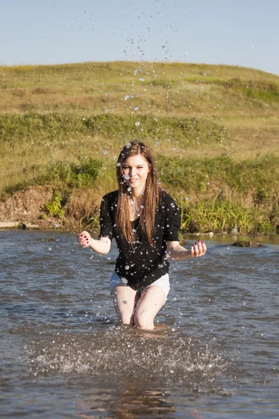 Hermosa chica con el pelo largo y liso posando y jugando con agua en un pequeño río — Foto de Stock