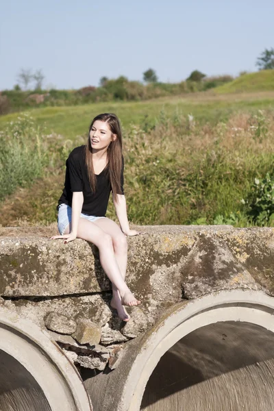 Hermosa chica con el pelo largo y liso posando y jugando en un puente de hormigón sobre un pequeño río — Foto de Stock