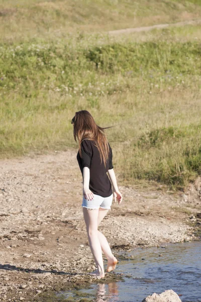 Beautiful girl with long, straight hair posing and playing with water in a small river — Stock Photo, Image