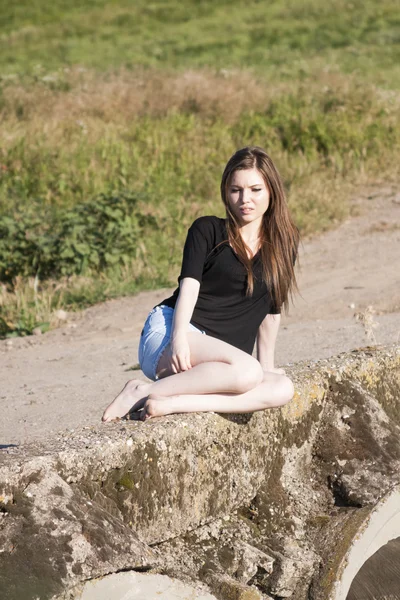 Beautiful girl with long, straight hair posing and playing on a concrete bridge over a small river — Stock Photo, Image