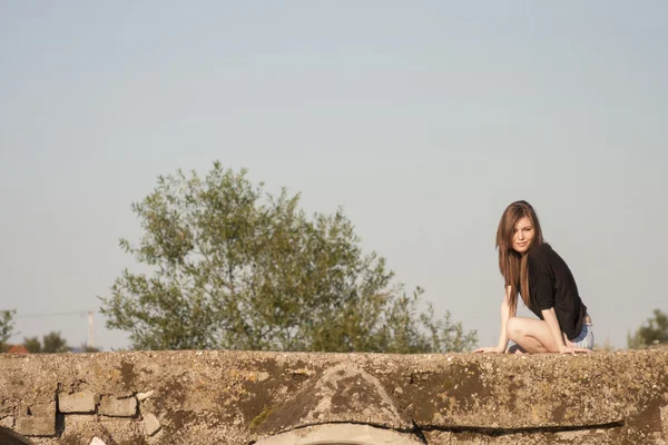 Hermosa chica con el pelo largo y liso posando y jugando en un puente de hormigón sobre un pequeño río — Foto de Stock