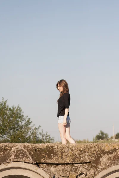 Krásná dívka s dlouhými, rovné vlasy, lodě a hrál na betonový most přes malé řeky — Stock fotografie