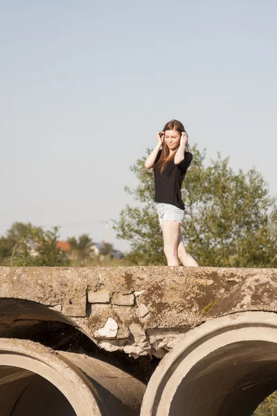 Красивая девушка с длинными прямыми волосами позирует и играет на бетонном мосту через маленькую реку — стоковое фото