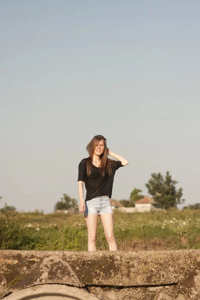 Beautiful girl with long, straight hair posing and playing on a concrete bridge over a small river — Stock Photo, Image