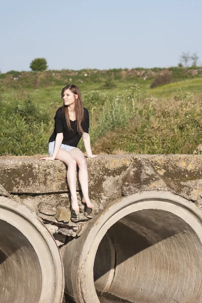 Beautiful girl with long, straight hair posing and playing on a concrete bridge over a small river — Stock Photo, Image