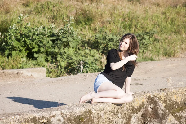 Hermosa chica con el pelo largo y liso posando y jugando en un puente de hormigón sobre un pequeño río — Foto de Stock