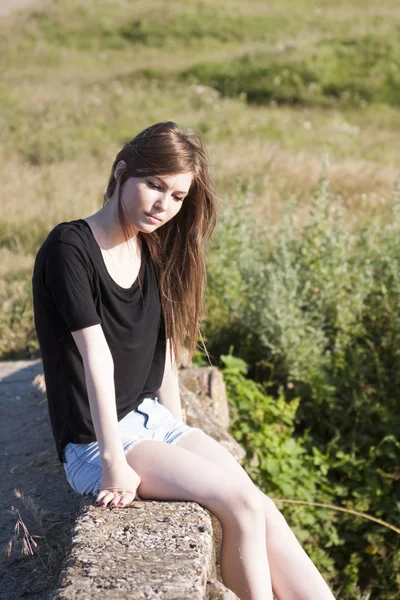 Hermosa chica con el pelo largo y liso posando y jugando en un puente de hormigón sobre un pequeño río — Foto de Stock