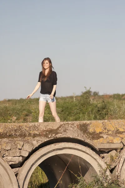 Mooi meisje met lange, rechte haren poseren en spelen op een betonnen brug over een kleine rivier — Stockfoto