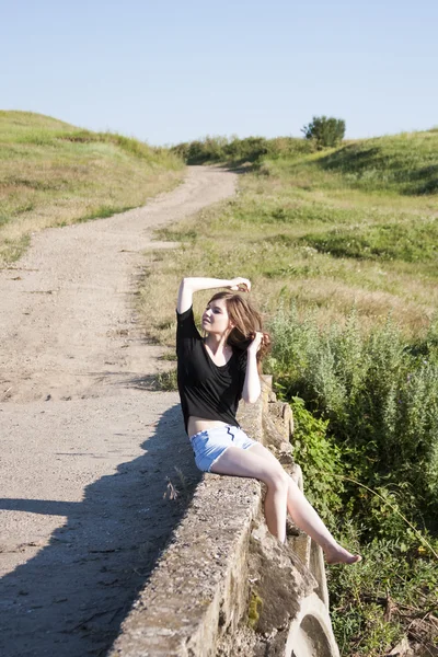 Hermosa chica con el pelo largo y liso posando y jugando en un puente de hormigón sobre un pequeño río — Foto de Stock