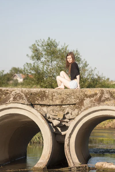 Krásná dívka s dlouhými, rovné vlasy, lodě a hrál na betonový most přes malé řeky — Stock fotografie