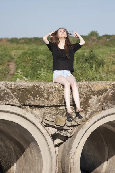 Hermosa chica con el pelo largo y liso posando y jugando en un puente de hormigón sobre un pequeño río — Foto de Stock