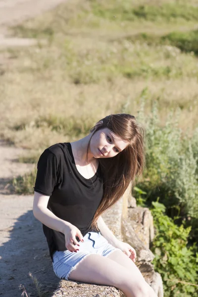 Красивая девушка с длинными прямыми волосами позирует и играет на бетонном мосту через маленькую реку — стоковое фото