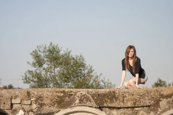 Hermosa chica con el pelo largo y liso posando y jugando en un puente de hormigón sobre un pequeño río — Foto de Stock