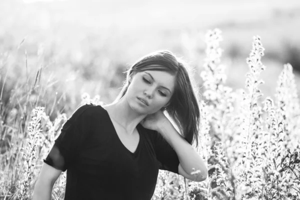 Black and white photo of beautiful girl with long, straight hair posing in the field looking melancholic