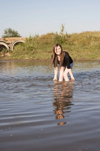 Hermosa chica con el pelo largo y liso posando y jugando con agua en un pequeño río — Foto de Stock