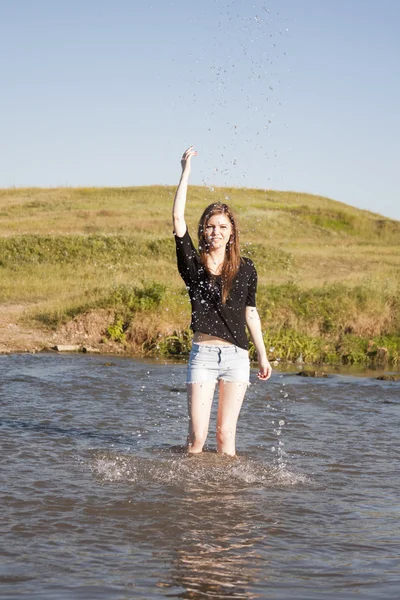 Belle fille aux cheveux longs et raides posant et jouant avec l'eau dans une petite rivière — Photo