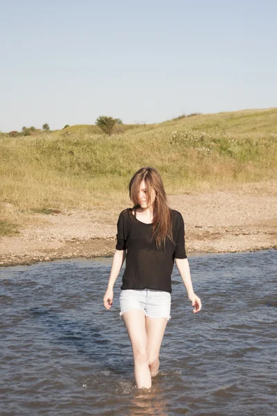 Belle fille aux cheveux longs et raides posant et jouant avec l'eau dans une petite rivière — Photo