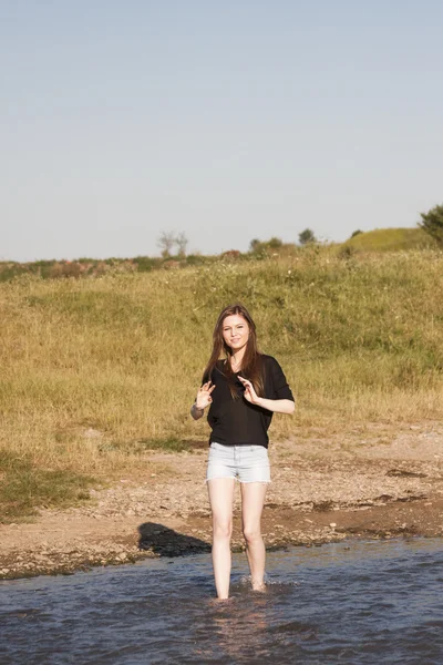 Девочка с длинными прямыми волосами позирует и играет с водой в маленькой реке — стоковое фото