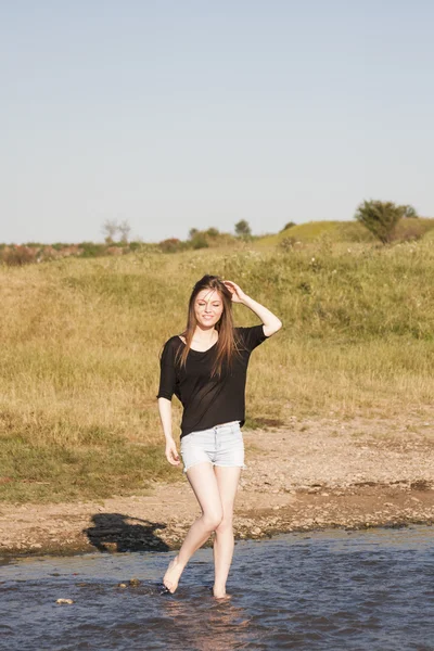 Vacker flicka med långa, raka hår poserar och leker med vatten i en liten flod — Stockfoto