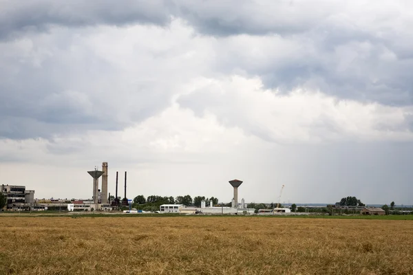 Industrial landscape with wheat field and dramatic clouds — Stock Photo, Image