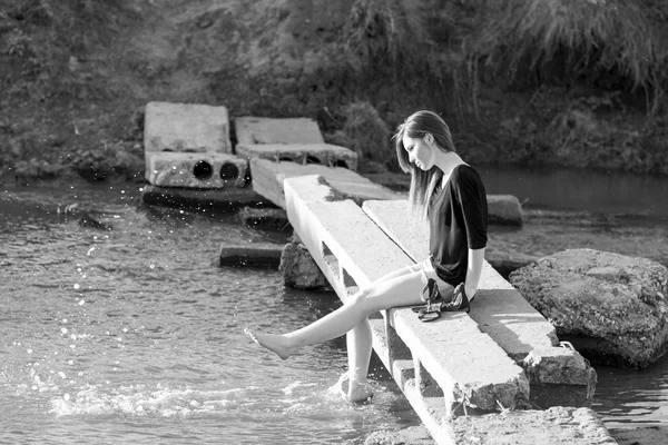 Hermosa chica con el pelo largo y liso posando y jugando con agua en un pequeño río. Blanco y negro, fotografía artística — Foto de Stock