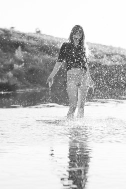 Poz ve küçük bir nehir su ile oynarken uzun, düz saçlı güzel kız. Siyah ve beyaz, sanatsal fotoğraf