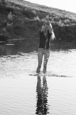 Poz ve küçük bir nehir su ile oynarken uzun, düz saçlı güzel kız. Siyah ve beyaz, sanatsal fotoğraf