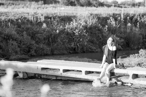 Hermosa chica con el pelo largo y liso posando y jugando con agua en un pequeño río. Blanco y negro, fotografía artística — Foto de Stock