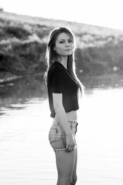 Hermosa chica con el pelo largo y liso posando y jugando con agua en un pequeño río — Foto de Stock