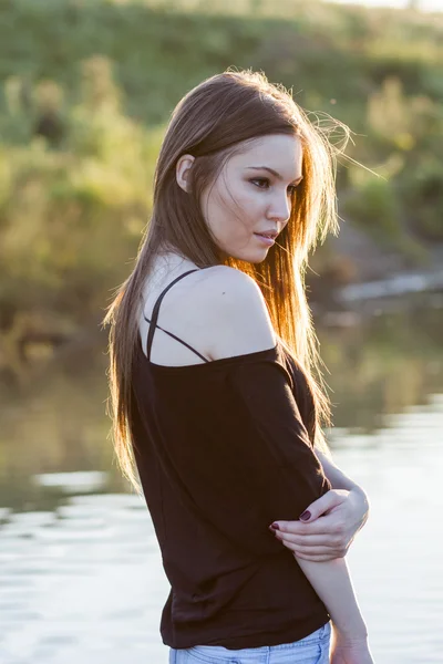 Bella ragazza con lunghi capelli dritti in posa nel campo con la luce del tramonto, contro la luce — Foto Stock