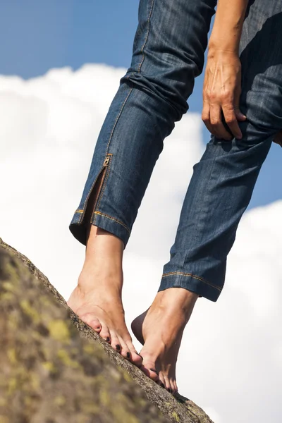 Женщина ноги, ноги и руки с джинсами, на скале, с естественным фоном и пушистыми, белые облака — стоковое фото