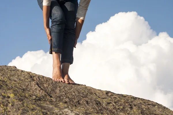 Donna gambe, piedi e mani con jeans, su una roccia, con sfondo naturale e soffice, nuvole bianche — Foto Stock