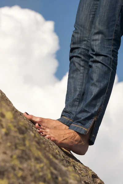 Woman legs, feet and hands with jeans, on a rock, with natural background and fluffy, white clouds — Stock Photo, Image