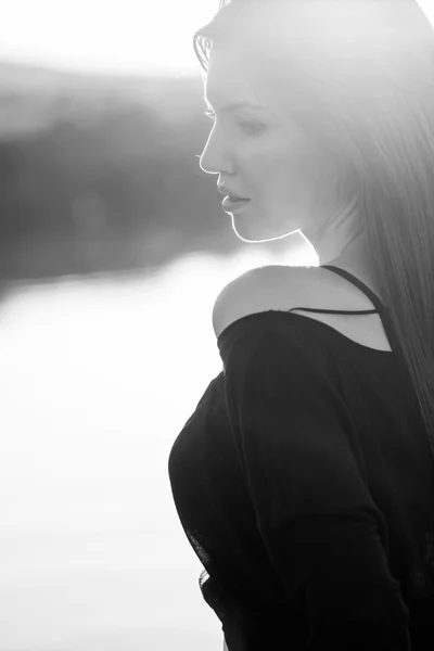 Menina bonita com cabelos longos e lisos posando no campo com luz do pôr do sol, contra a luz — Fotografia de Stock