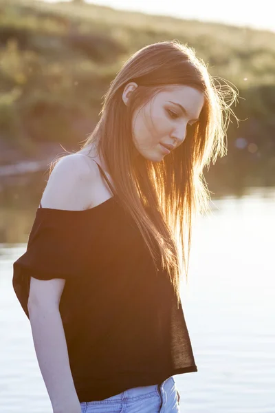 Hermosa chica de pelo largo y liso posando en el campo con luz del atardecer, contra la luz — Foto de Stock