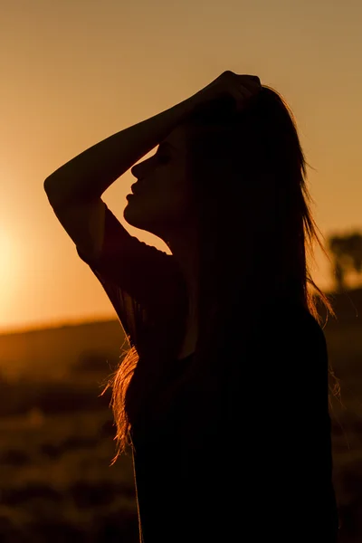 Hermosa chica de pelo largo y liso posando en el campo con luz del atardecer, contra la luz — Foto de Stock